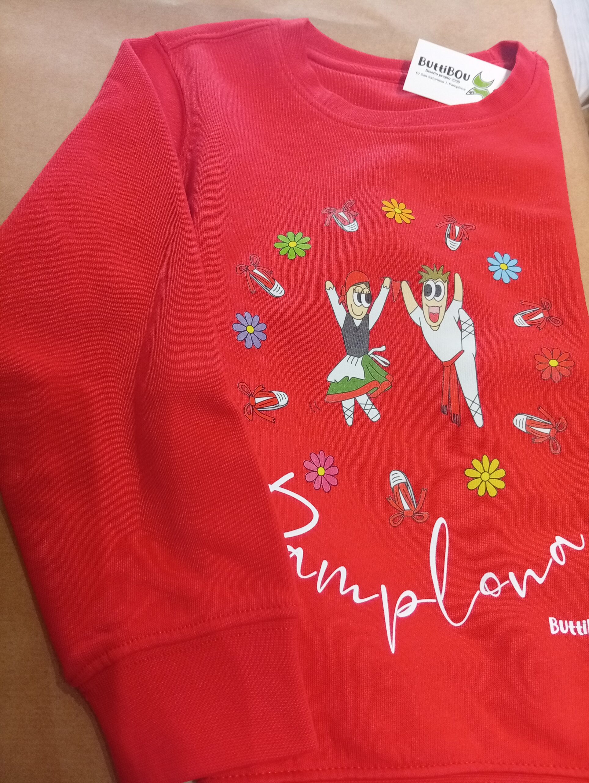 Sudadera de algodón orgánico con estampación de dantzaris en colores rojo, verde y naranja, divertida y cómoda, por ButtiBou Pamplona. Organic cotton sweatshirt with Dantzaris print in red, green, and orange, fun and comfy, by ButtiBou Pamplona Sudadera infantil/adulto de algodón orgánico con estampación de dantzaris, disponible en rojo, verde y naranja, diseño exclusivo de ButtiBou Pamplona. Organic cotton sweatshirt for kids/adults with Dantzaris print, available in red, green, and orange, exclusive design by ButtiBou Pamplona