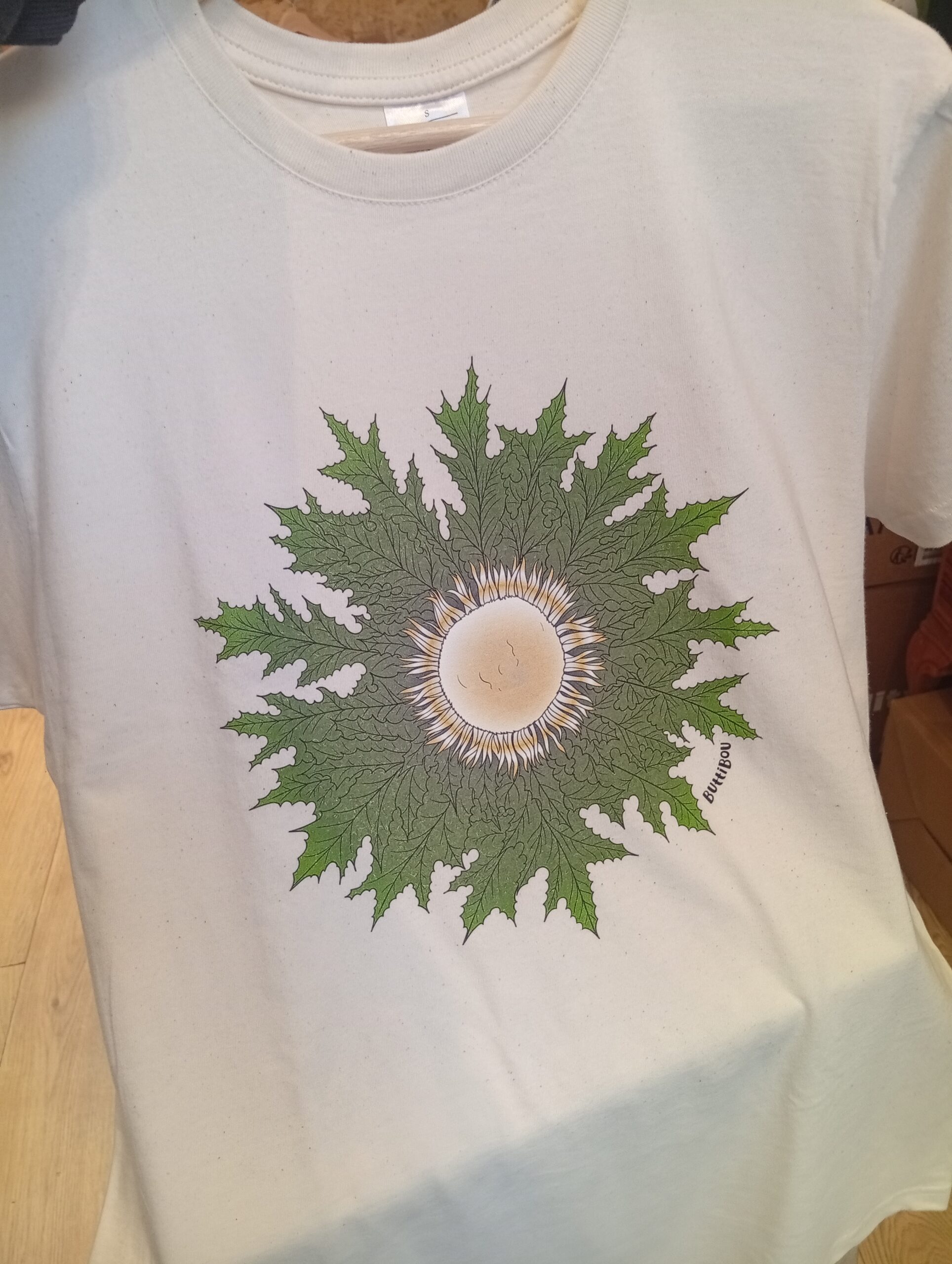 Camiseta Eguzkilore color natural – comodidad, estilo y tradición navarra en una prenda única de ButtiBou Pamplona. camiseta Eguzkilore color natural de ButtiBou Pamplona, símbolo navarro de protección inspirado en la flor del sol