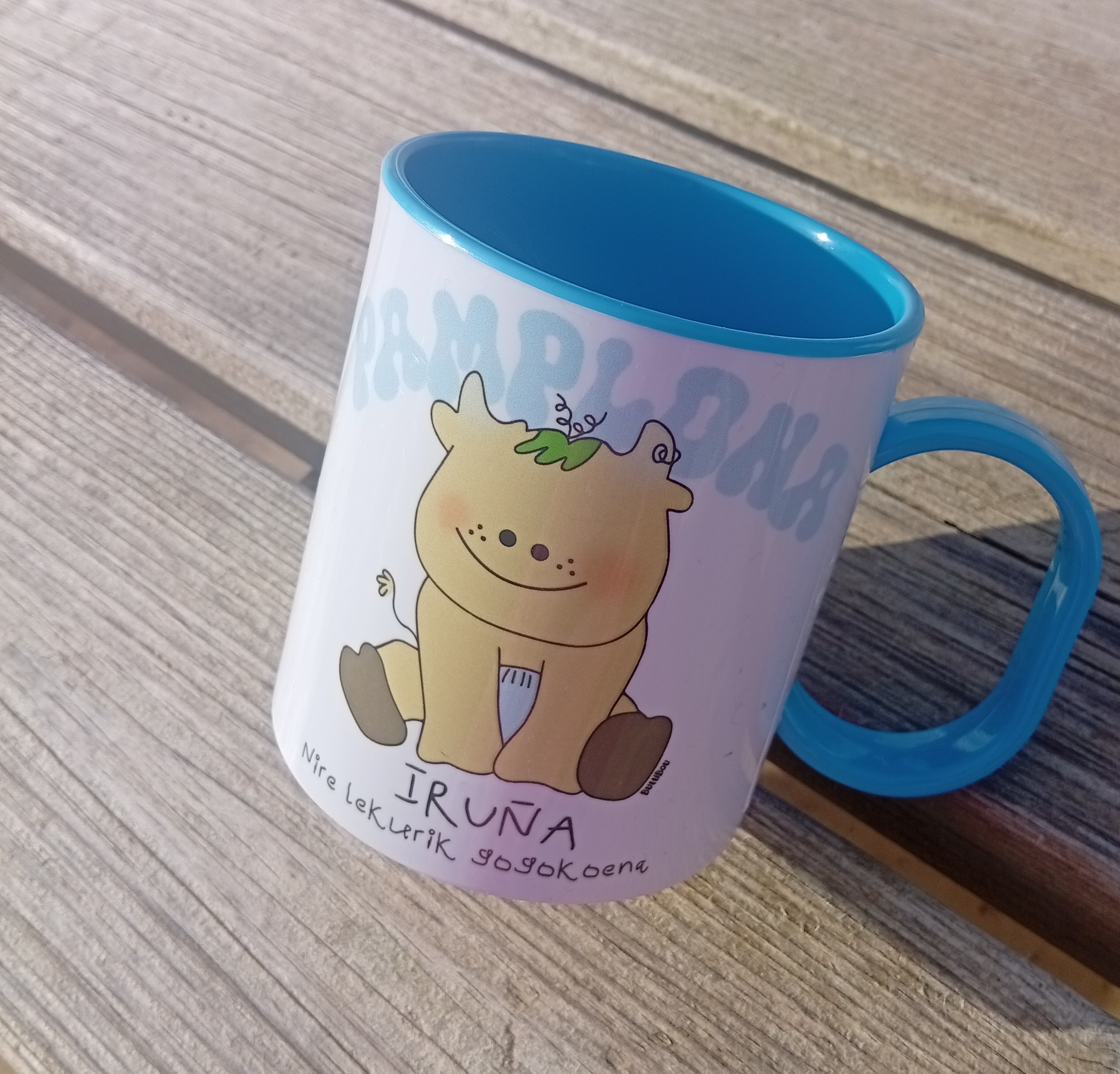 Taza infantil de plástico con interior azul claro y diseño de un becerrito. Texto: “Pamplona, mi lugar favorito”. Ideal para los más pequeños y su bebida favorita. Light blue plastic children’s mug with a cute calf design and text: “Pamplona, my favorite place”. Perfect for kids’ drinks. Light blue plastic children’s mug with a calf and text “Pamplona, my favorite place / Iruña nire lekurik gogokoena”, exclusive ButtiBou Pamplona design. Taza infantil de plástico azul con becerrito y texto “Pamplona, mi lugar favorito / Iruña nire lekurik gogokoena”, diseño exclusivo ButtiBou Pamplona.