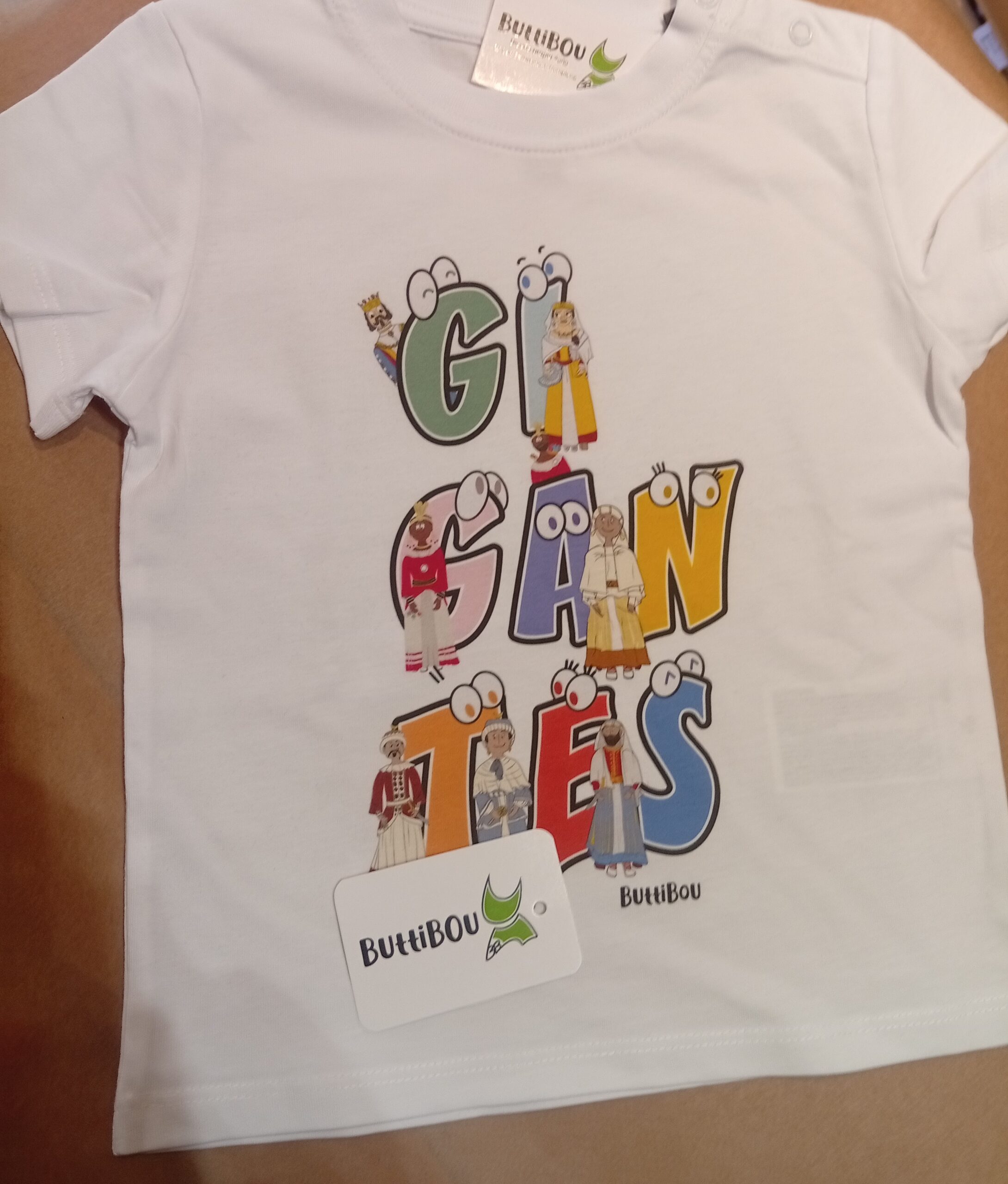 Camiseta infantil blanca con la palabra “Gigantes” formada por unos gigantes muy coloridos de Pamplona. White children’s T-shirt featuring the word “Gigantes” with each letter as a Pamplona giant character.White children’s T-shirt with colorful “Gigantes of Pamplona” design forming the word Gigantes. Camiseta infantil blanca con estampado colorido de los Gigantes de Pamplona formando la palabra Gigantes.