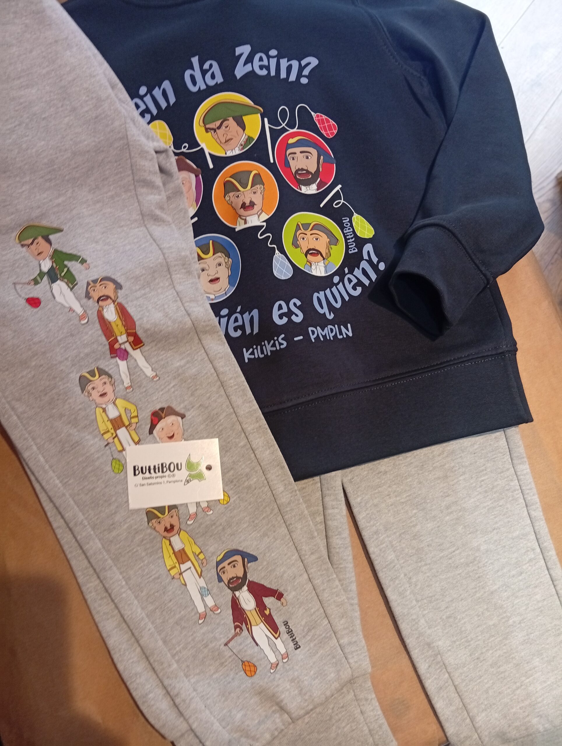 Conjunto infantil “Quién es quién” Kilikis de ButtiBou Pamplona, divertido y cómodo, sudadera azul y pantalón gris estampado. “Quién es quién” children’s Kilikis outfit by ButtiBou Pamplona, fun and comfy, blue sweatshirt and printed grey trousers Conjunto infantil “Quién es quién” Kilikis de Pamplona con sudadera azul de algodón orgánico y pantalón gris afelpado estampado de kilikis y vergas de colores. “Quién es quién” children’s Kilikis outfit from Pamplona with blue organic cotton sweatshirt and grey fleece trousers printed with Kilikis and colorful Vergas