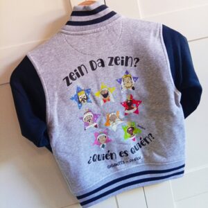 Sudadera High School con interior gris claro, mangas azules, dobladillo, cuello y puños de canalé bicolor. Estampación espalda “Quién es Quién – Gigantes de Pamplona” y delantero “Gigantes JoseMiguelErico y JosePhamunda”. High School sweatshirt with light gray interior, blue sleeves, bicolor ribbed hem, collar, and cuffs. Back print “Quién es Quién – Pamplona Giants” and front print “Gigantes JoseMiguelErico and JosePhamunda”.