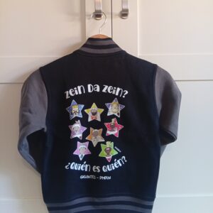 Sudadera estilo High School con dobladillo inferior, cuello y puños a rayas bicolor, mangas en contraste, botones a presión y estampación “Quién es Quién – Gigantes de Pamplona” en la espalda y “Yo amo los gigantes” delante. High School style sweatshirt with bicolor ribbed hem, cuffs, and collar, contrasting sleeves, snap buttons, and “Quién es Quién – Pamplona Giants” print on the back and “I Love the Giants” on the front.