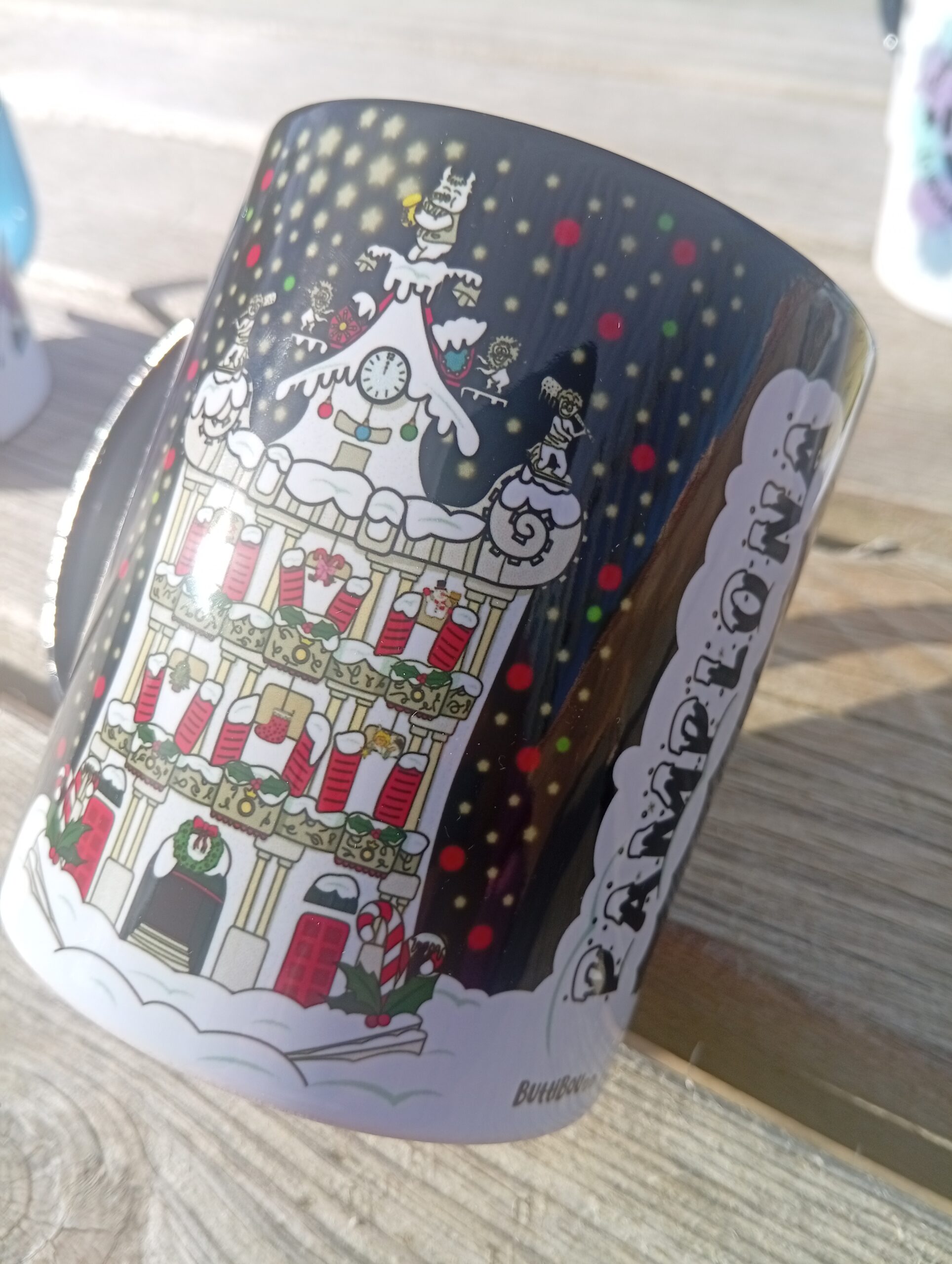 La Plaza Consistorial de Pamplona brilla en Navidad en esta taza de porcelana con interior negro. Pamplona’s City Hall Square shines at Christmas on this black-interior porcelain mug. Taza de porcelana con interior negro y diseño navideño de la Plaza Consistorial de Pamplona decorada con nieve y luces, diseño exclusivo de ButtiBou Pamplona. Porcelain mug with black interior featuring a Christmas design of Pamplona’s City Hall Square decorated with snow and lights, exclusive ButtiBou Pamplona design.