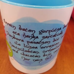 Taza Lamia Txikia con ilustración de Lamia entre nenúfares y peces, diseño ButtiBou Pamplona. Lamia Txikia mug featuring the Lamia among water lilies and fish, ButtiBou Pamplona design.